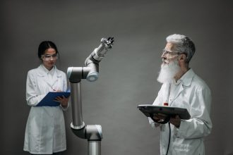 Dois cientistas trabalham com um braço robótico em um laboratório.