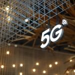 Placa iluminada com a inscrição “5G” em um ambiente interno de arquitetura moderna.