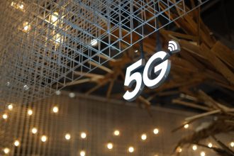 Placa iluminada com a inscrição “5G” em um ambiente interno de arquitetura moderna.