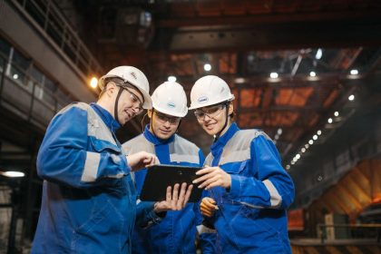 Grupo de engenheiros discute um projeto em um tablet dentro de uma fábrica.